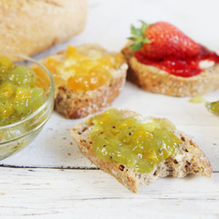kiwi, orange and strwberry jam with slices of bread on wooden ta