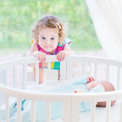 Cute toddler girl playing with her newborn baby brother in a bed