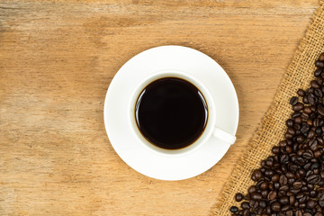 Coffee cup and roasted beans over hessian on wooden table