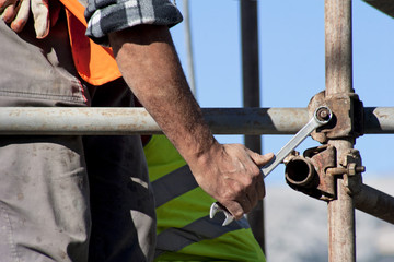 Worker with wrench builds scaffolding on construction site