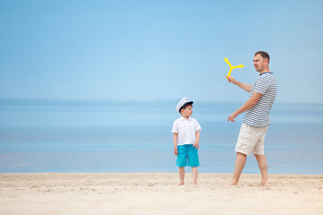 Father and son playing together on the beach - obrazy, fototapety, plakaty