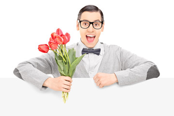 Happy male holding flowers behind a panel