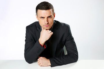 Confident businessman sitting at the table over gray background