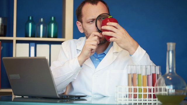 Biochemist examine red pepper, writing results on laptop