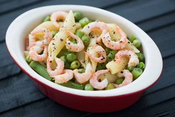 Penne with shrimps, peas and beans, black wooden background