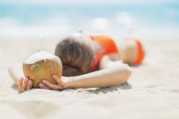 Young woman with coconut relaxing on beach