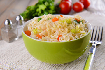Tasty instant noodles with vegetables in bowl on table close-up
