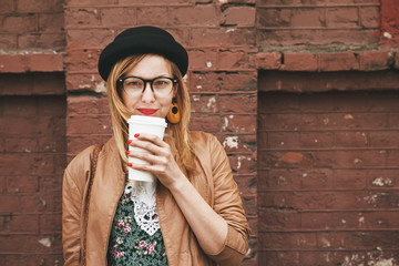 stylish woman drinking coffee on brick wall background