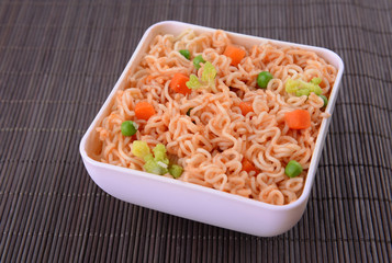 Tasty instant noodles with vegetables in bowl on table close-up