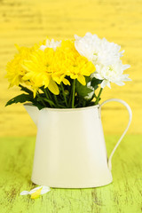 Beautiful chrysanthemum flowers in pitcher on wooden table