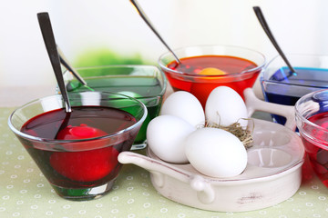 Eggs with liquid colour in glass on table on bright background