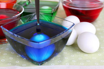 Eggs with liquid colour in glass bowls on table close up