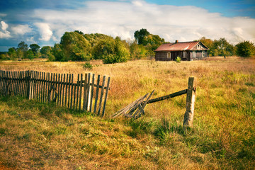 Old house with wooden fence on the empty meadow - 63253428