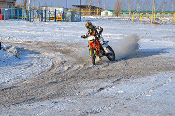 MX rider on motorcycle moves in a turnabout with skid in snow