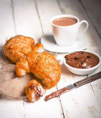Fresh baked croissants with chocolate cream and hot cocoa on woo