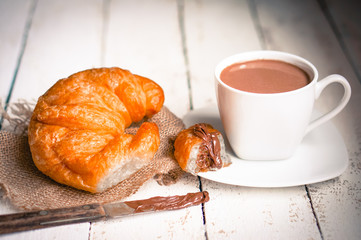 Fresh baked croissants with chocolate cream and hot cocoa on woo
