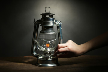 Hand lights a kerosene lamp on dark grey background