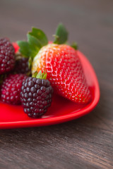 red juicy strawberry and blackberry in red plate on a wooden sur