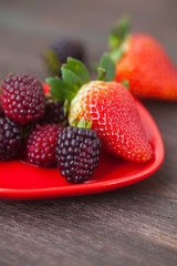 red juicy strawberry and blackberry in red plate on a wooden sur