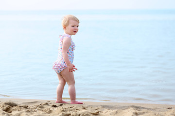 Fototapeta na wymiar Cute toddler girl in colorful spotty swimsuit playing on beach