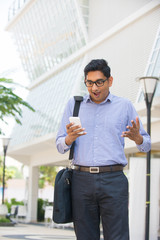 shocked looking indian business male on a smartphone with office
