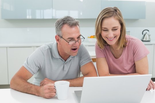 Couple using laptop while man drinking coffee in kitchen
