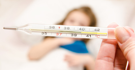 Mother holding thermometer foreground and sick little girl