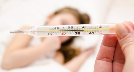 Mother holding thermometer foreground and sick little girl