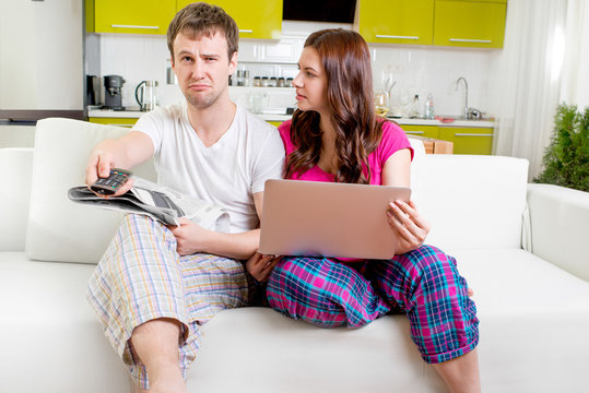Young married couple in pajamas sitting in the sofa with newspap
