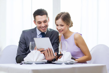 couple with menus on tablet pc at restaurant
