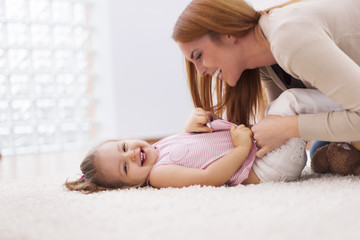 Loving mother tickling her little girl on carpet at home - obrazy, fototapety, plakaty