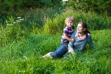 Naklejka na ściany i meble Little boy and his mother sitting on grass in summer forest