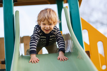 Fototapeta na wymiar Adorable toddler boy having fun and sliding on outdoor playgroun