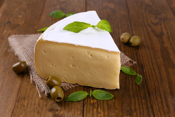 Tasty Camembert cheese with basil and olives, on wooden table