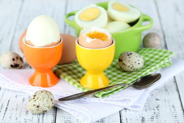 Boiled eggs in pan and eggcup on color wooden background