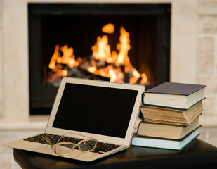 laptop and pile of books against the background of the fireplace © Ermolaev Alexandr