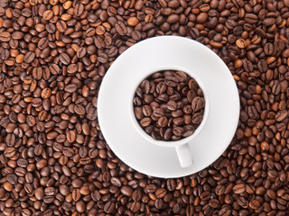 A white cup with many coffee beans on coffe background
