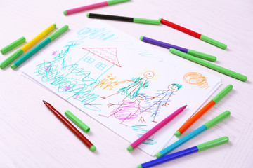 Kids drawing of family and colored pencils on wooden table