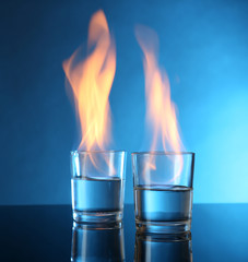 Glasses with burning alcohol on blue background