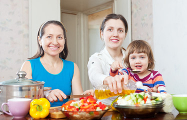  woman and adult daughter with girl cooking salad