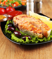 Tasty grilled salmon with lemon and vegetables, on wooden table