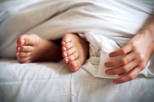 Sleeping child barefoot feet and hand on white bed linen. Indoor