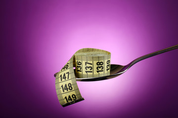 Measuring tape in silver spoon on purple background
