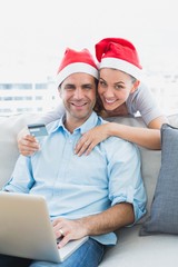 Happy couple in santa hats shopping online with laptop