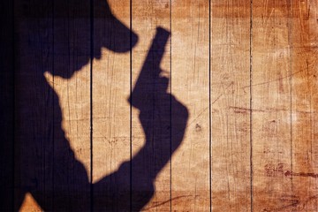 Man with a gun in shadow on a wooden background