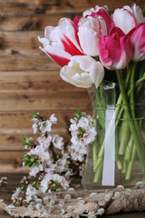 Beautiful tulips in glass jug on wooden background