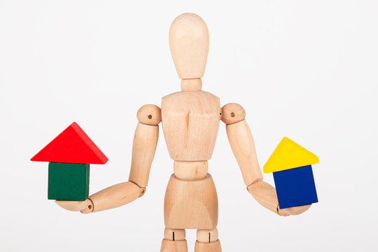 Small wood mannequin sit holding colourful block house isolated