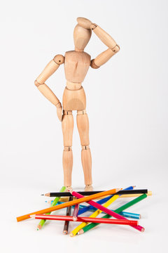 Confused wood mannequin standing at heap of colour pencil isolat