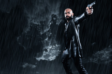 Fototapeta na wymiar Dangerous bald gangster man with beard holding gun. Wearing blac