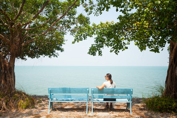 Fototapeta premium Young woman sitting on bench facing the sea